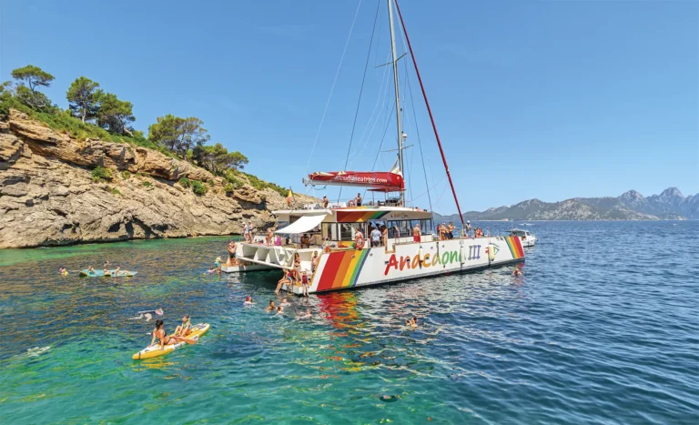 Passengers on a catamaran tour in Mallorca swimming, paddle boarding and snorkeling next to a catamaran anchored in a cove in Alcúdia