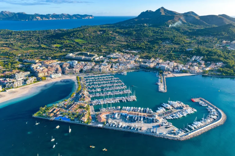 Puerto de Alcúdia con barcos y el malecón, Mallorca Vista del Puerto de Alcúdia con las embarcaciones amarradas en el malecón y las instalaciones portuarias y la ciudad al fondo, Mallorca