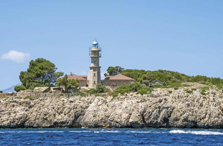 Phare de la Punta de l'Avançada à Port de Pollença, Majorque Le phare de la Punta de l'Avançada sur les rochers d'une petite péninsule stratégique à l'entrée du port naturel de la baie de Pollença. La Fortaleza d'Albercuix, une construction défensive, est visible aux alentours, avec la mer bleue en arrière-plan, Majorque